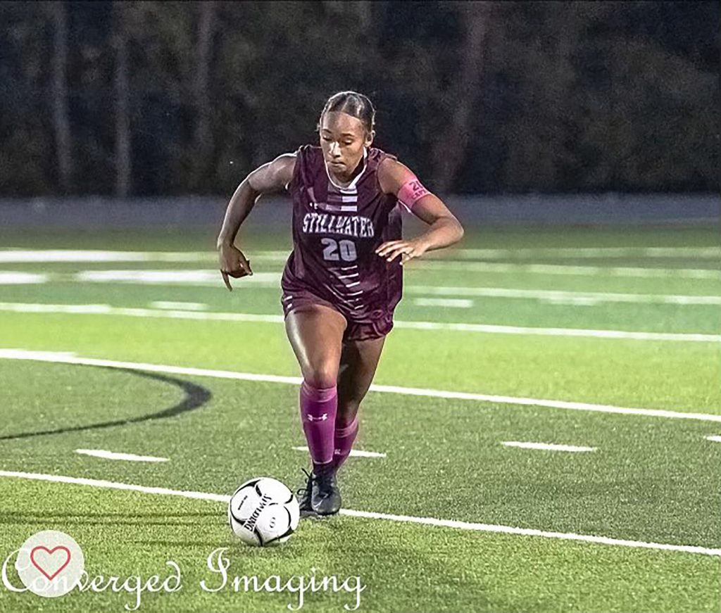 Girl soccer player running on field with a soccer ball at her feet.