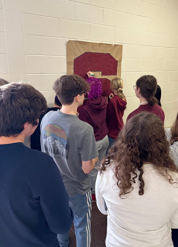 Students signing giant "S" hanging on wall.