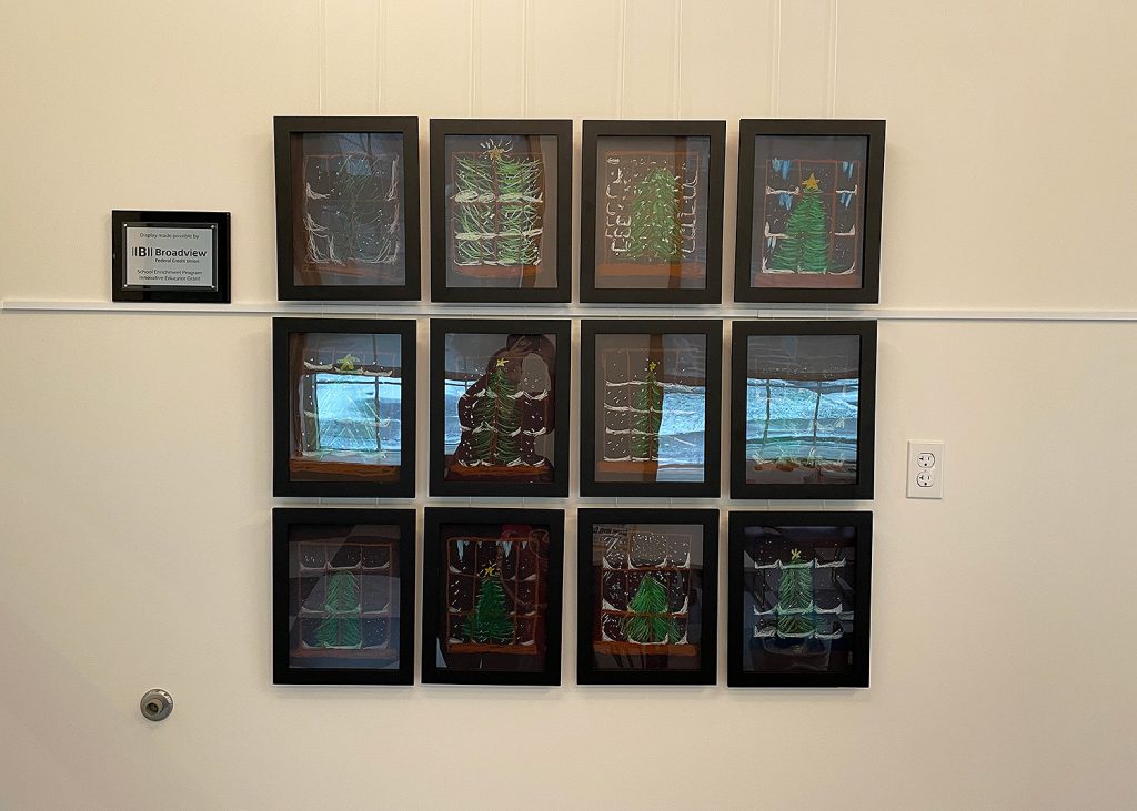Twelve frames hanging on a wall containing student artwork.