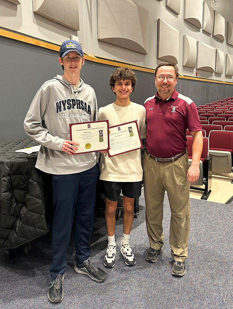 Two student athletes and their coach standing and smiling for a photo.