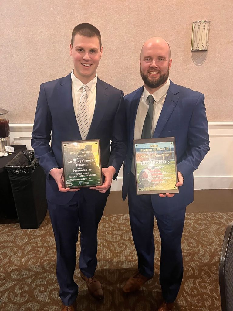 Varsity student athlete and coach smiling for a photo together. Each is holding their respective award plaques in their hands.
