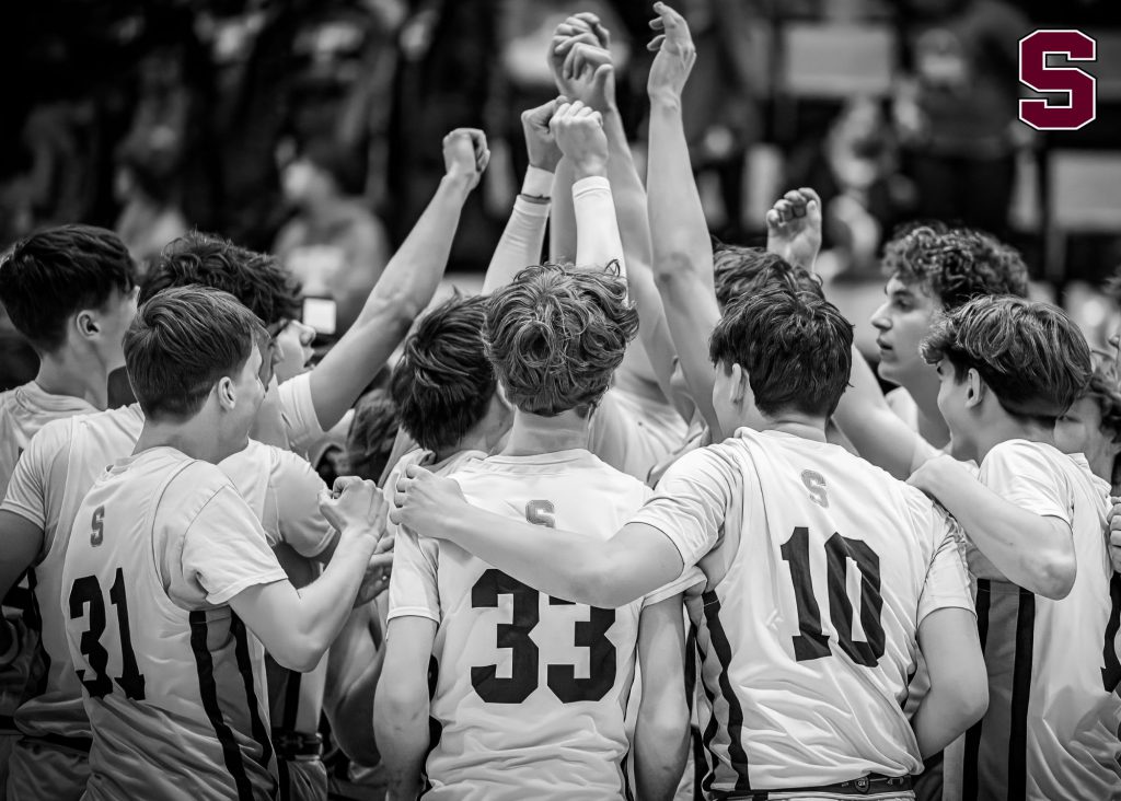 Boys varsity basketball team putting their hands up in the air together.