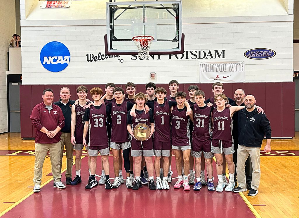 Boys varsity basketball team standing on court for group photo holding championship plaque.