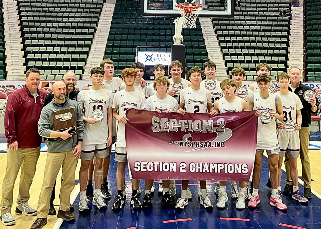 Group photo of varsity basketball team and coaches holding championship banner.