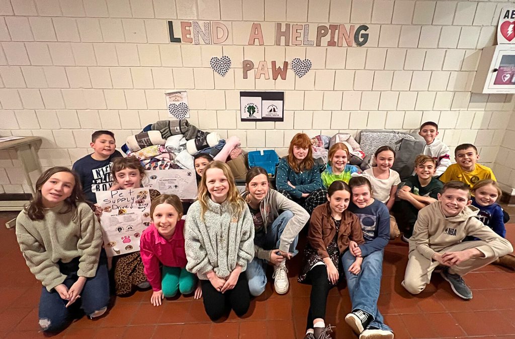 Elementary students sitting in front of boxes filled with donated pet items. 