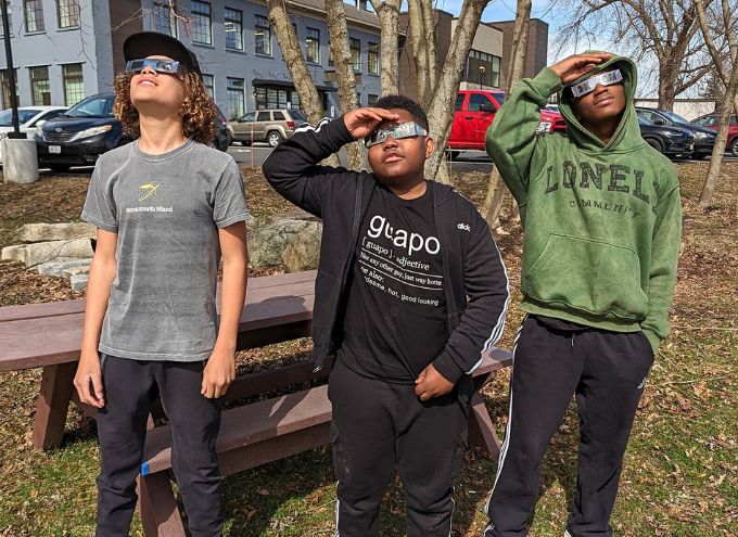 Three students wearing eclipse glasses looking up at the sky.