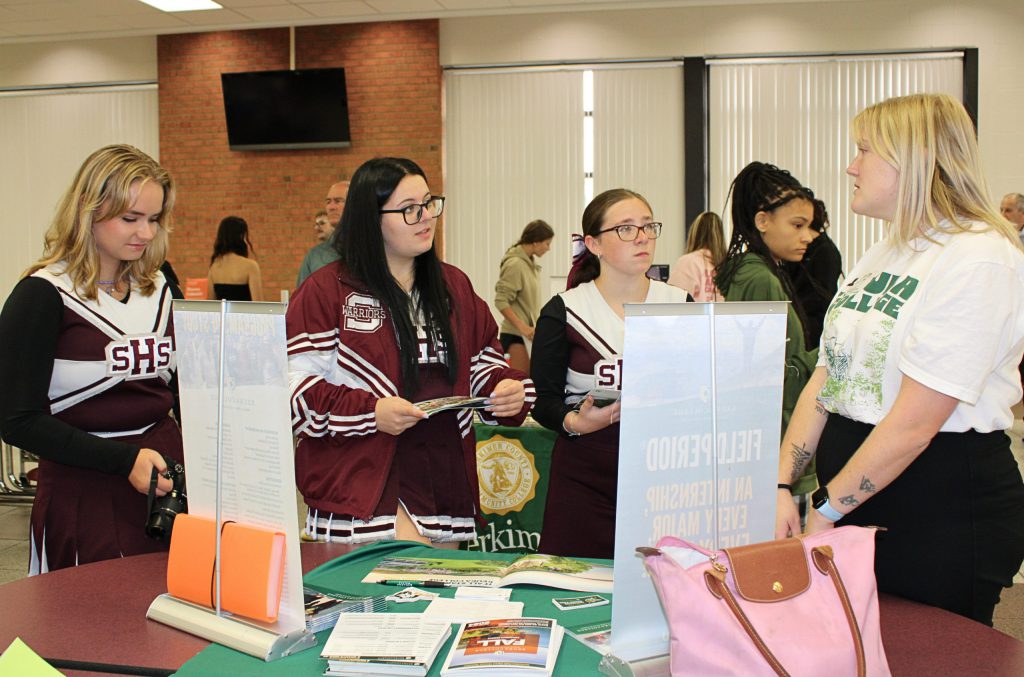 Three students listening to an adult at the end of a table.