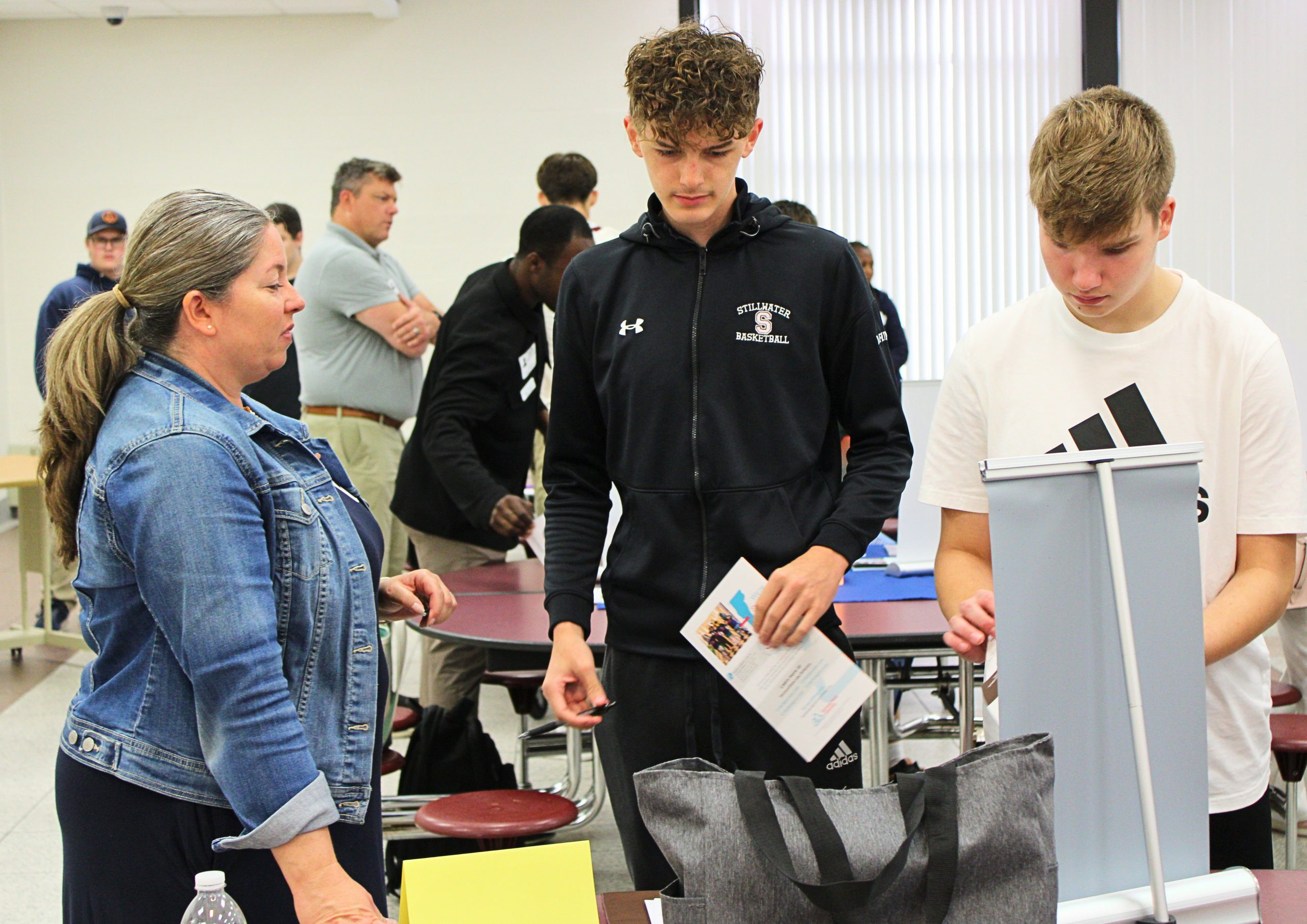 Two students invested in a poster as an adult talks with them.