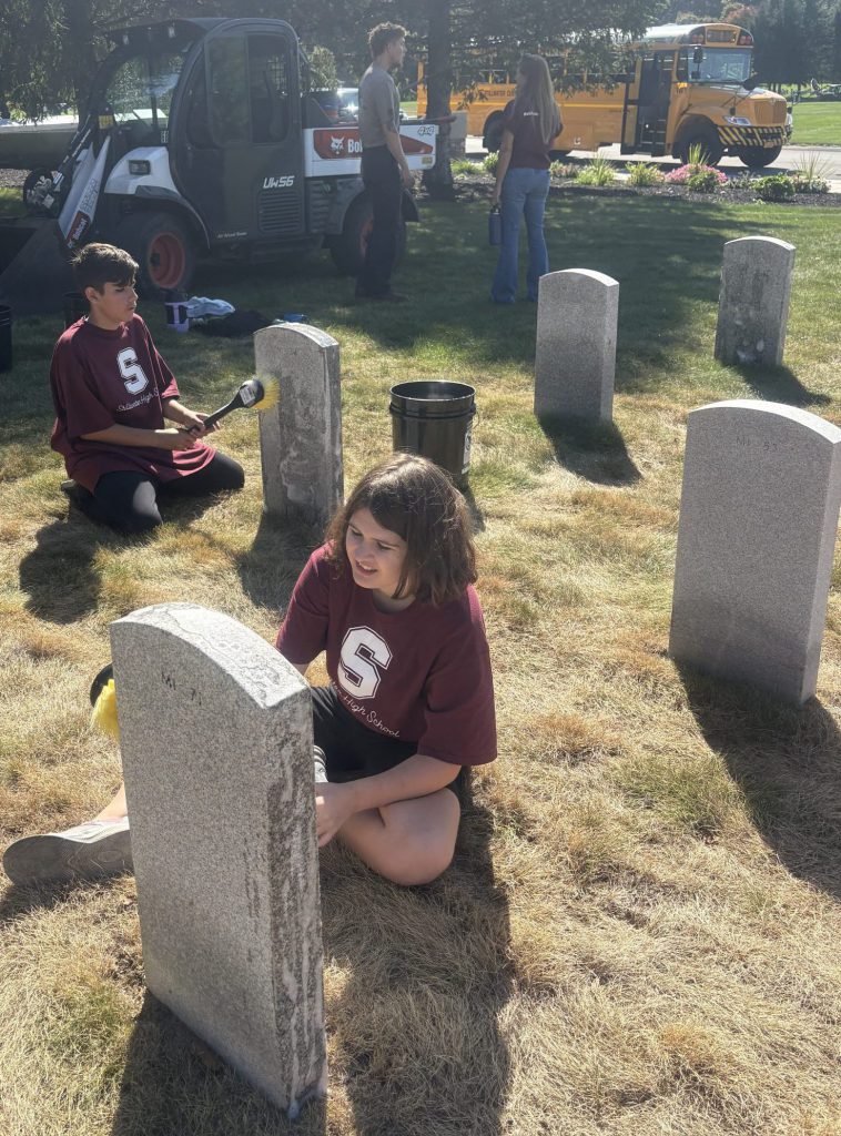 Students sitting and cleaning tombstones with yellow brushes.
