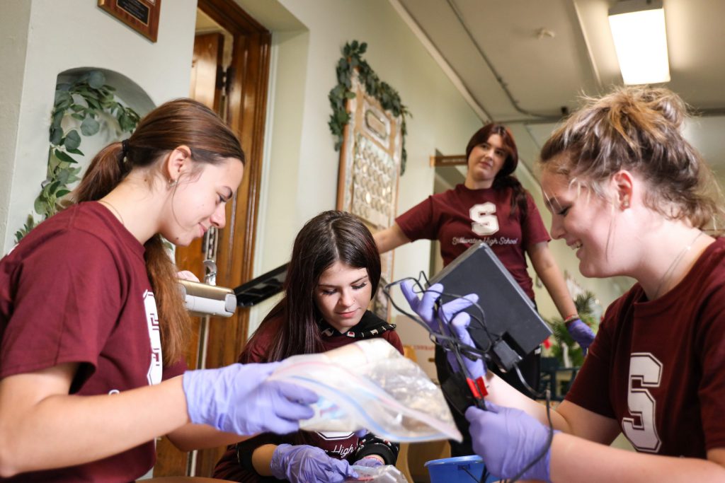 4 students on the ground inspecting items with gloves on.