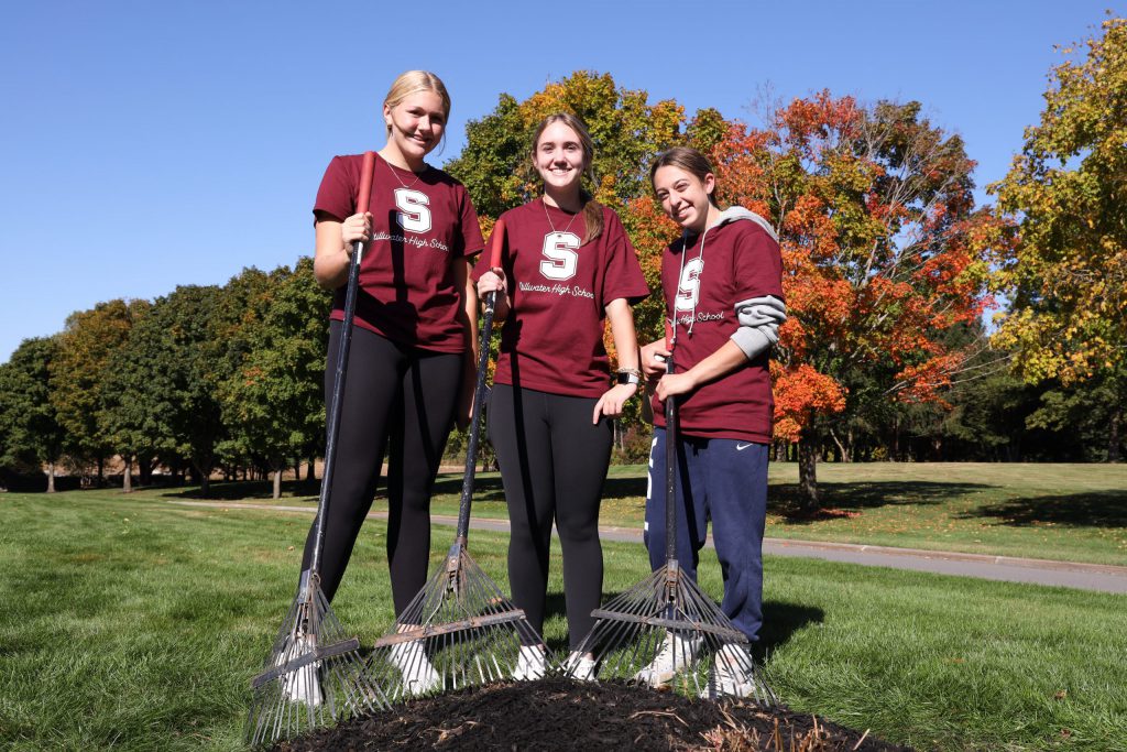 3 Students in matching Stillwater shirts smiling with rakes in hand.