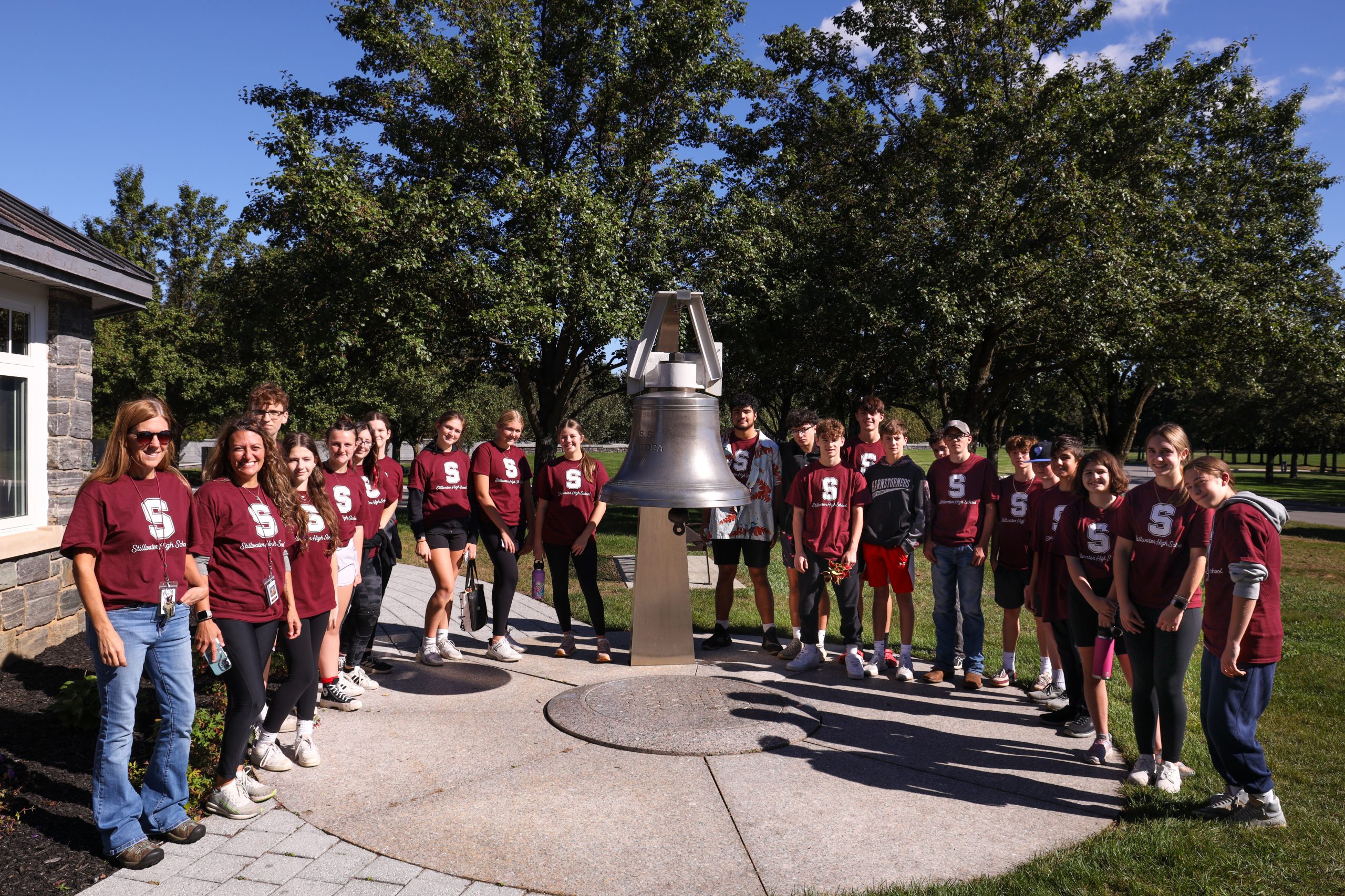 Students in matching shirts circling a bell.