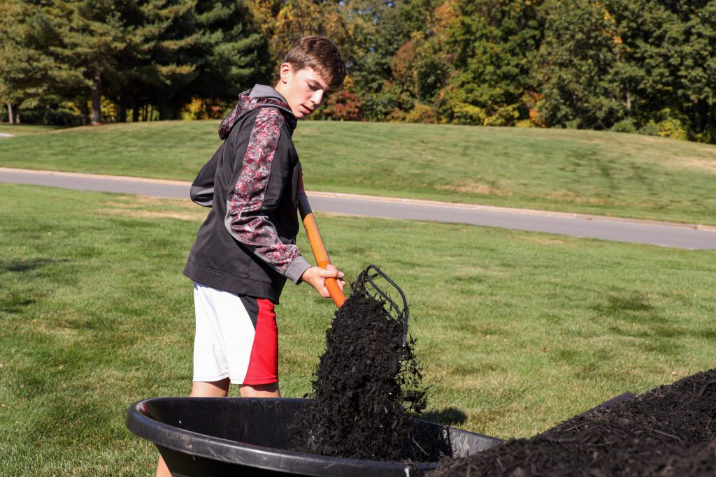 Student shoveling dirt into a bin.