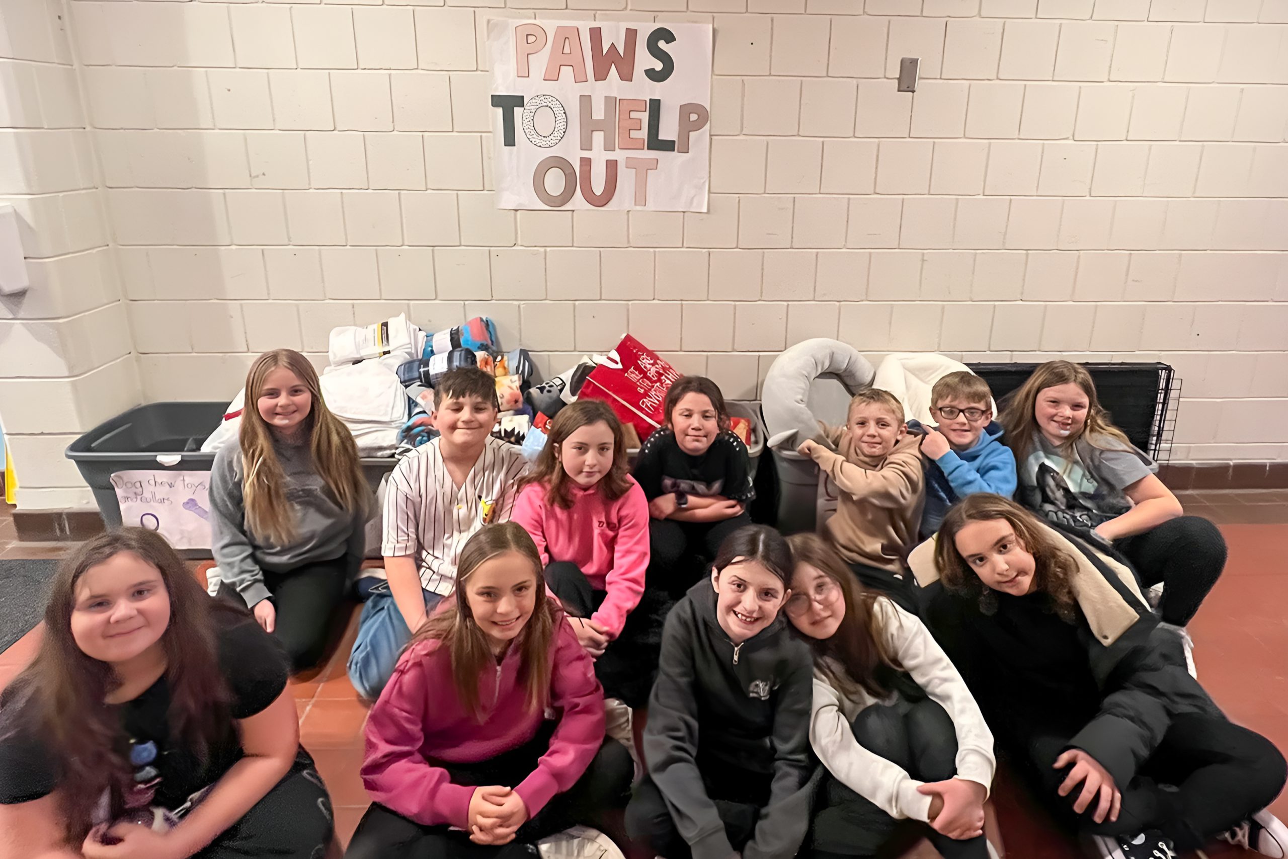 Group of students smiling sitting on the ground in front of donations for PAWS TO HELP OUT.