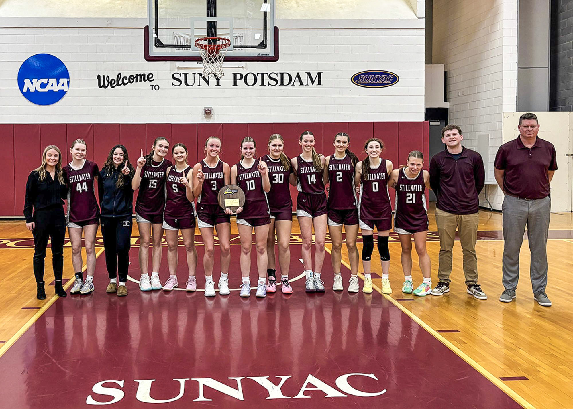 Group of Athletes smiling together in matching uniforms with two holding some award.