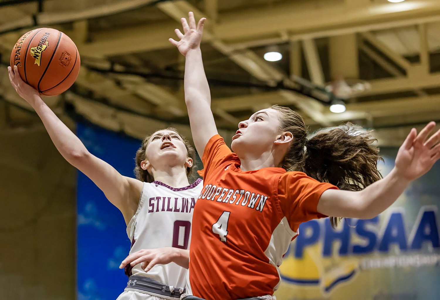 Two athletes in air, one attempting to block a basketball from the other.
