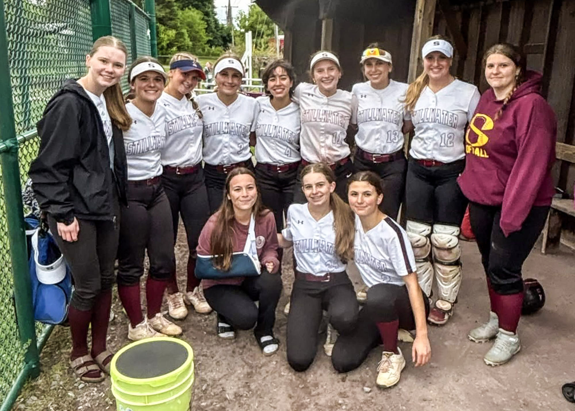 Group of athletes huddled together in dugout smiling at the camera.