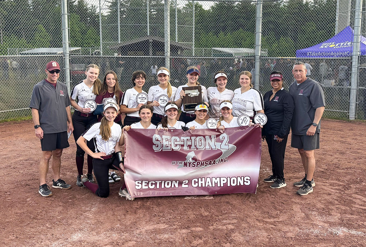 Athletes and coach smiling holding a banner stating "Section 2 Champions"