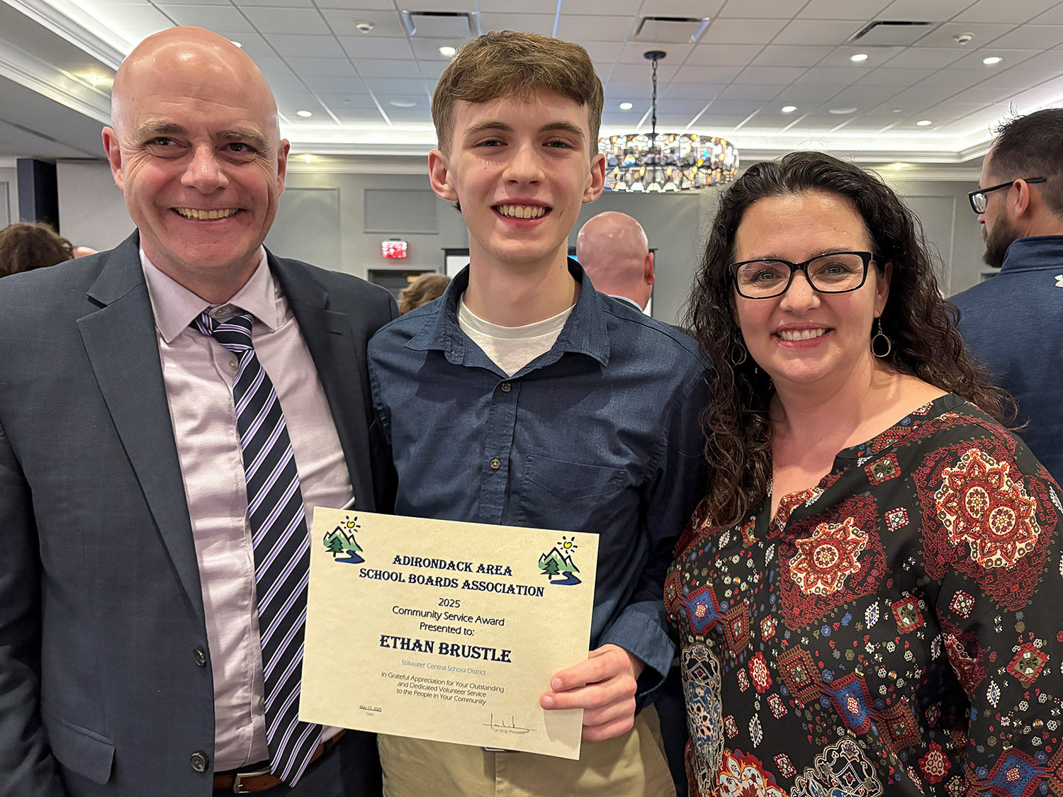 Ethan Brustle AASBA Award Recipient smiling and holding certificate with two adults smiling proud.