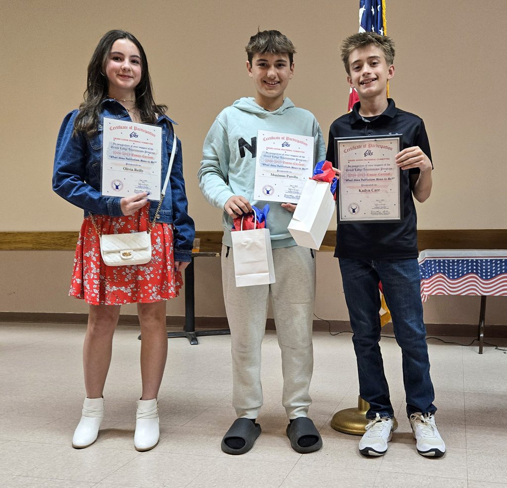 Three students holding certificates and gift bags while smiling for a photo.