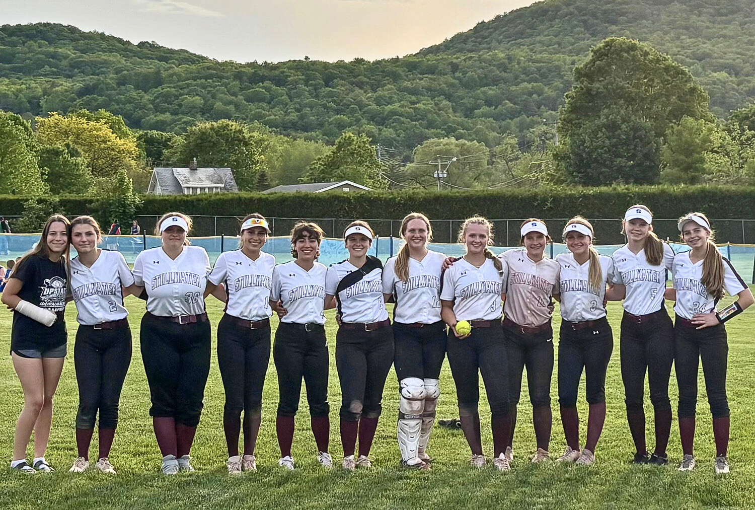 Group of athletes in matching attire smiling in a photo as one holds a softball.