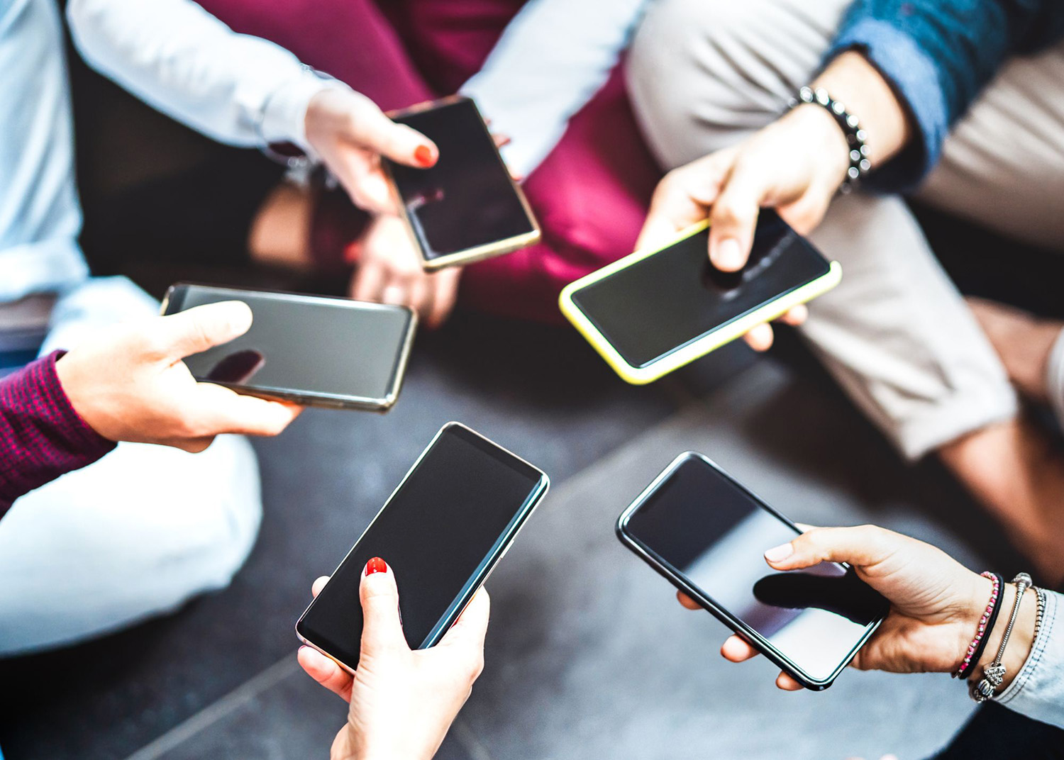 Six people are sitting in a circle, each holding a smartphone with their screens facing up.