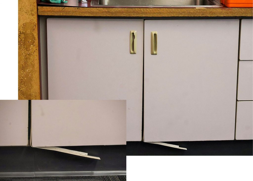 An image showing two photos of casework in a classroom. The large photo in the back shows the damaged casework as a whole, including the cabinets, handles, countertop and splintered bottom. The up close image in the bottom left is an up close shot of the splintered casework at the bottom.