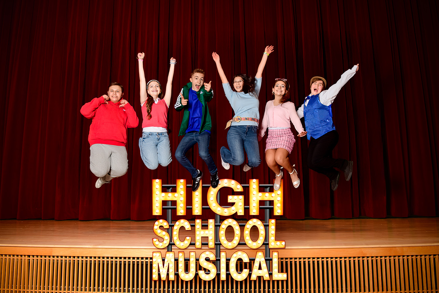 Six students jumping in the air on stage with the text "High School Musical" below them.