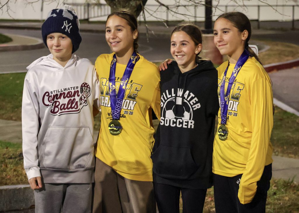 Four middle schoolers smiling for a photo. Three are young girls and one is a boy. Two of the girls are wearing long sleeve yellow shirts and medals around their necks.