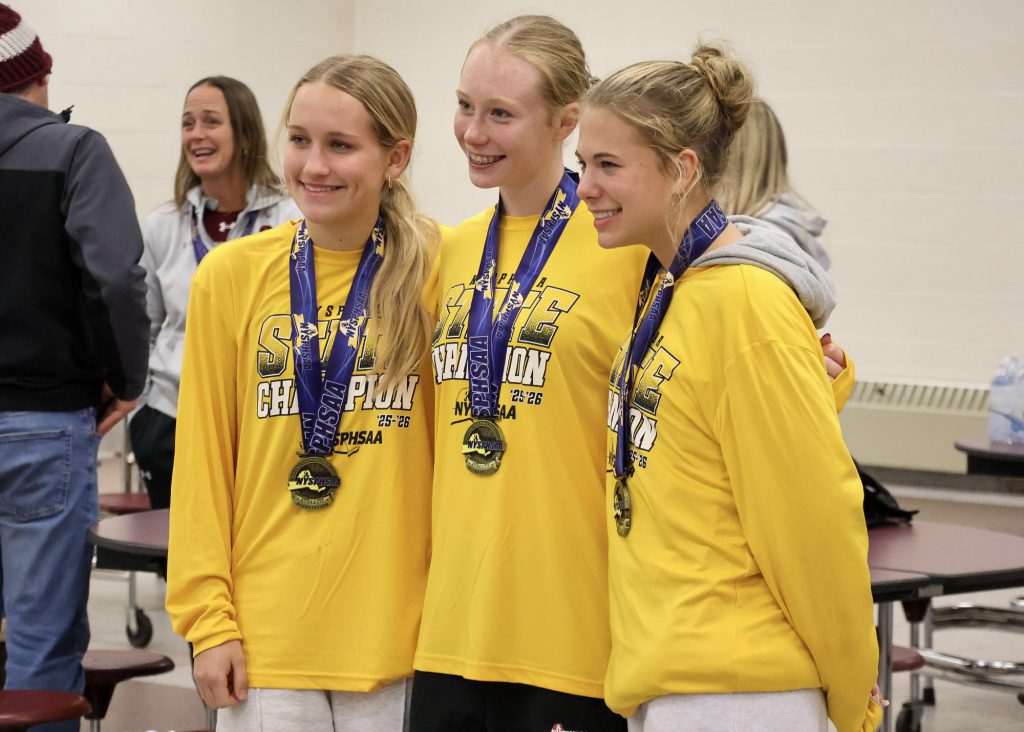 Three female soccer players wearing long sleeve yellow shirts and medals around their necks, smiling for a photo.