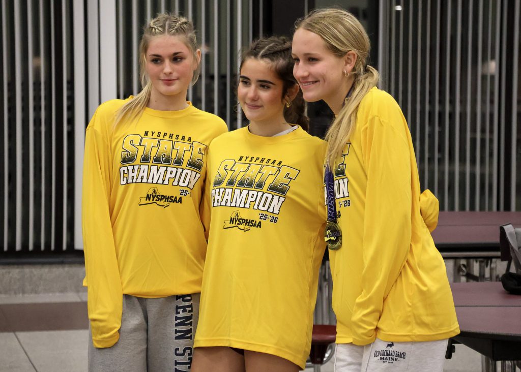 Two female soccer players wearing long sleeve yellow shirts, smiling for a photo. The player on the right is wearing a medal around her neck.