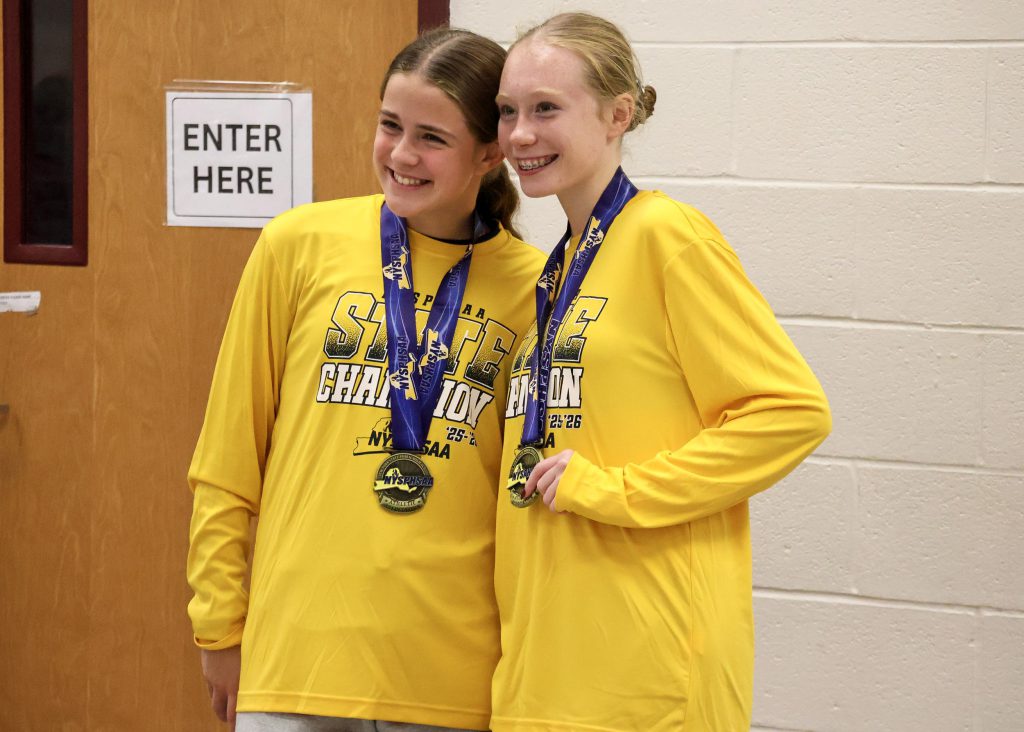 Two female soccer players wearing long sleeve yellow shirts and medals around their necks, smiling for a photo.