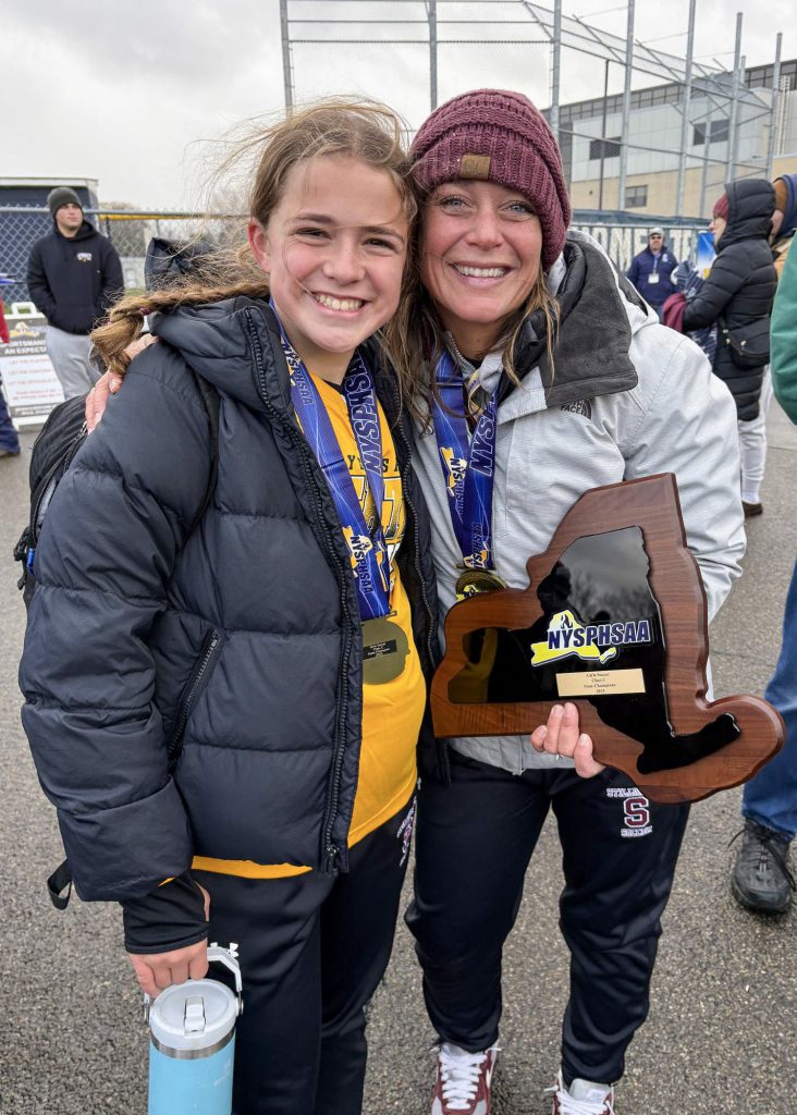 Coach and a player smiling for a photo together. The coach is holding a plaque shaped like New York State and it says "NYSPHSAA" on it.