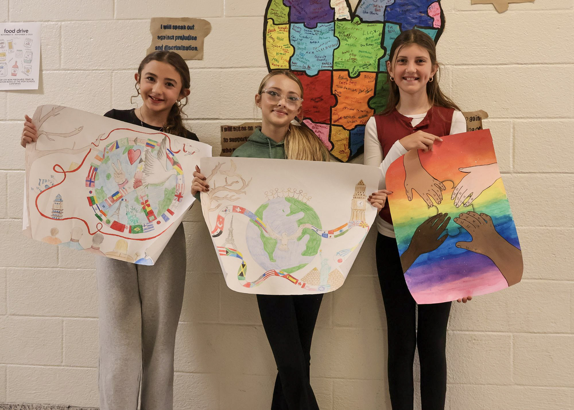 Three middle school students holding their handmade posters and smiling for a group photo. The three young ladies each drew a poster representing world peace.