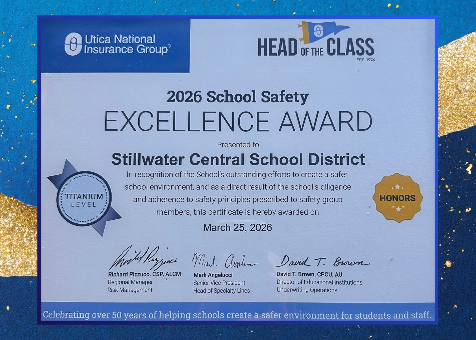 2026 School Safety Excellence Award presented to Stillwater Central School District, recognizing the school's outstanding efforts to create a safer environment for students and adherence to safety principles. The certificate is awarded on March 25, 2026. The district earned Titanium level with honors. There are three signatures at the bottom of individuals associated with Utica National Insurance Group who award the certificate.
