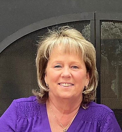 Woman with blonde short hair wearing a purple shirt, smiling towards the camera.