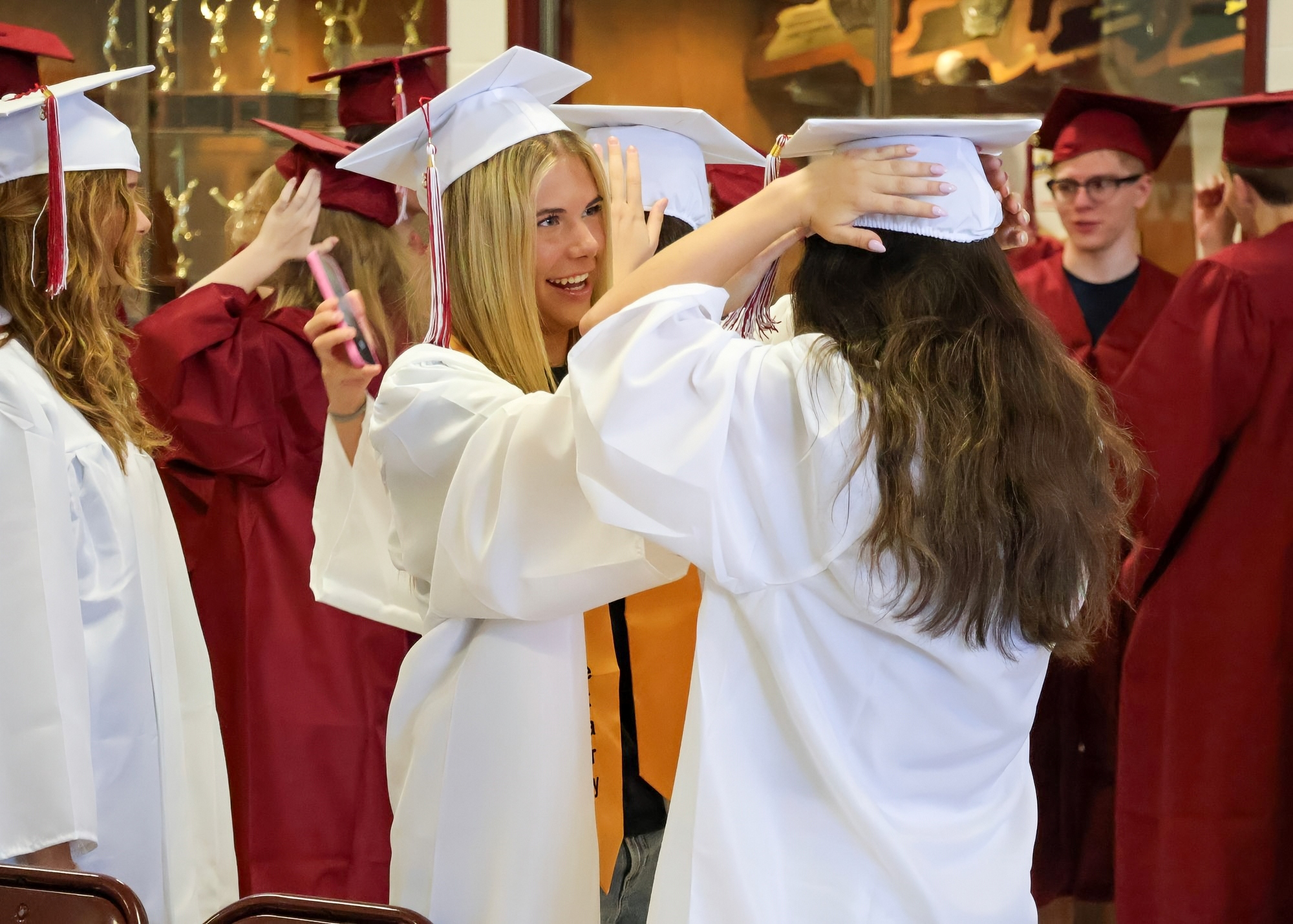 Two female graduates wearing white caps and gowns, adjusting their caps.