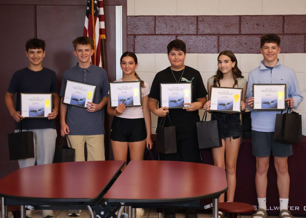 A group of six students holding certificates and gift bags, standing in front of a maroon/white wall with the Stillwater Central School District "S" logo in white. There are four boys and two girls.