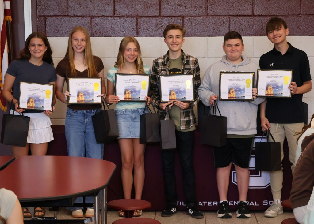 A group of six students holding certificates and gift bags, standing in front of a maroon/white wall with the Stillwater Central School District "S" logo in white. There are three boys and three girls.