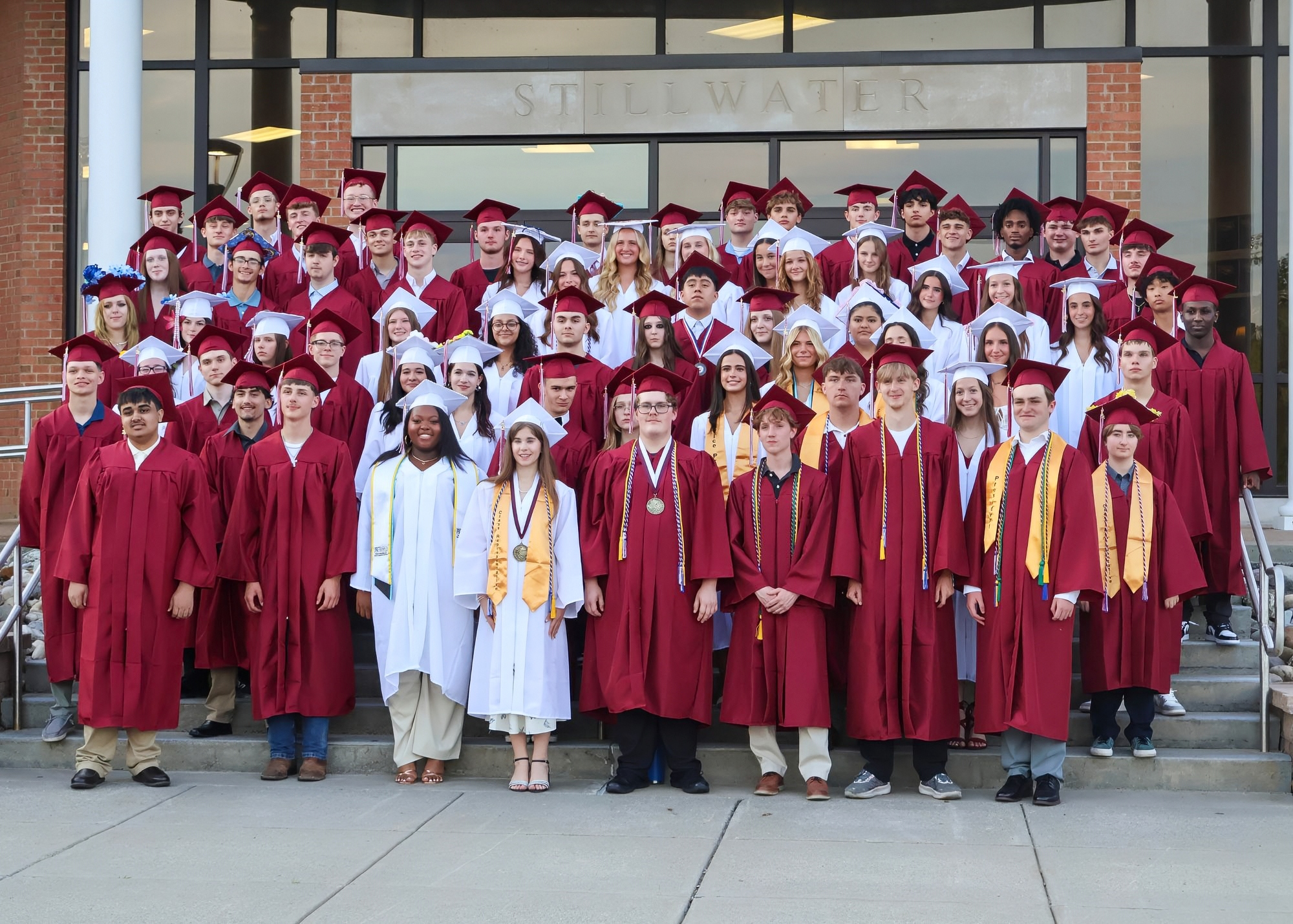 A large group of graduates wearing red caps and gowns posing together in front of a building.
